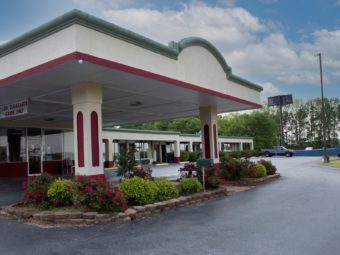 Hotel entrance with drive through canopy, landscaping with flowering shrubs, grassy areas and parking spaces