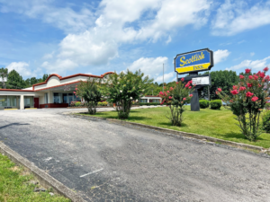 Brand signage, landscaping with grassy area and shrubs, hotel canopied entrance