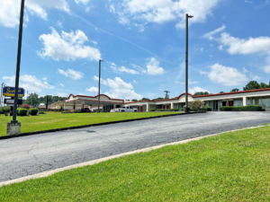 Hotel entrance, one story building, covered walkways with exterior guest room entrances, grassy areas, parking spaces