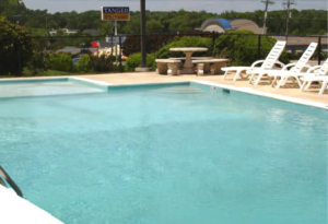 Outdoor seasonal pool, concrete poolside with pool loungers, stone table and benches