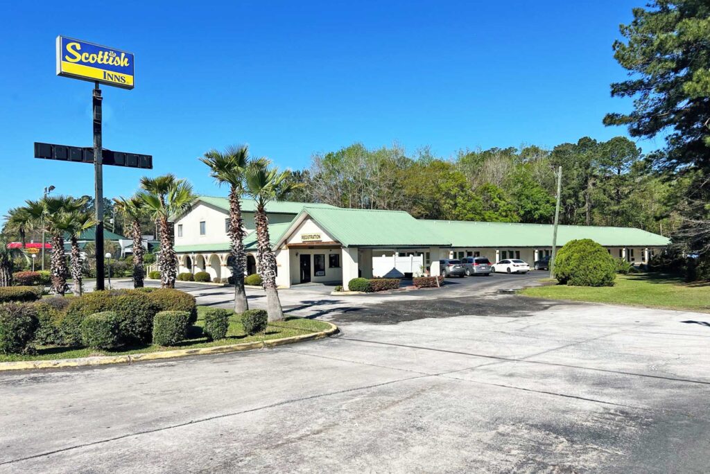 Hotel entrance with drive through canopy, exterior entrances to guest rooms with covered walkway, parking spaces, brand signage, landscaping with small shrubs and trees