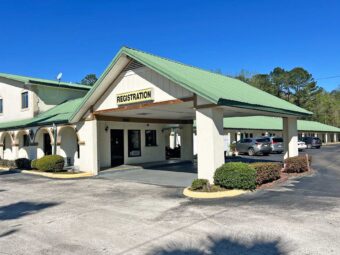 Hotel entrance with drive through canopy, exterior entrances to guest rooms with covered walkway, parking spaces, landscaping with small shrubs