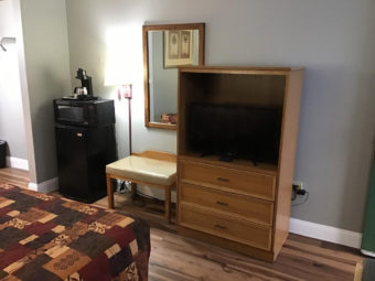 Queen bed, fridge with microwave and coffee maker, wall mounted light and mirror, wooden tv console with flat screen tv, upholstered stool, laminate flooring