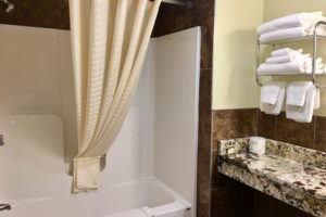 Shower tub with shower curtain and bath mat, vanity unit, shelves with towels