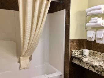 Shower tub with shower curtain and bath mat, vanity unit, shelves with towels