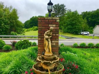 Fountain, flowering shrubs, shrubs, grassy area, brick post with lamp