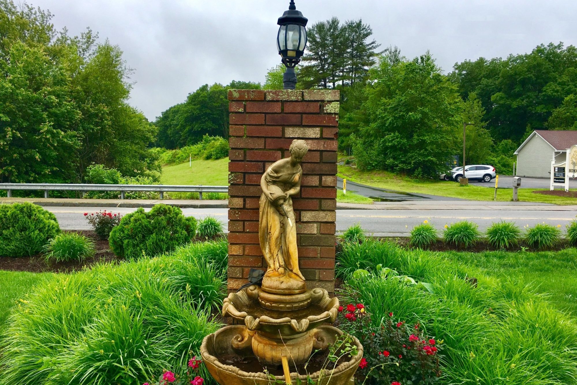 Fountain, flowering shrubs, shrubs, grassy area, brick post with lamp