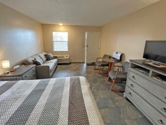 Queen bed, wooden drawer unit with bedside lamp and telephone, sofa, small table and chairs, wooden drawer unit with flatscreen TV, tiled flooring