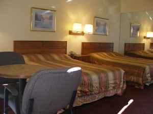 Two double beds, night stand with telephone, wall mounted bedside lights and art, small table and chairs, carpet flooring