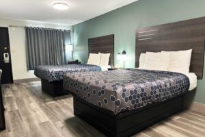 Two queen beds, nightstand with telephone, bedside lights, easy chair, floor lamp, laminate flooring