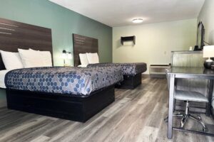 Two queen beds, night stand with telephone, bedside lights, desk with chair and table lamp, wooden unit with TV, hanging rail