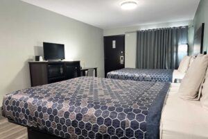 Two queen beds, night stand, floor lamp, wooden unit with TV, fridge and microwave, desk with chair