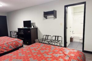 Double beds, desk with chair, wooden unit with TV, Fridge and microwave, portable folding luggage racks, hanging rail, doorway to bathroom with showertub, laminate flooring