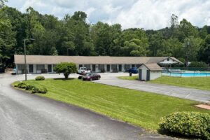 One story building with exterior guest room entrances, parking spaces, grassy area, outdoor pool