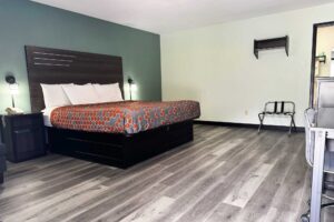 King bed, night stand with telephone, bedside lights. portable folding luggage rack, hanging rail, desk with chair, doorway to bathroom, laminate flooring