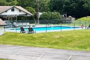 Outdoor pool surrounded by fence, grassy area, hotel in the background