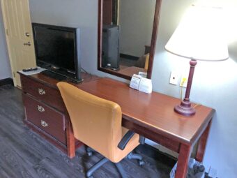 Wooden drawer unit with TV, desk with chair and lamp, mirror, laminate flooring