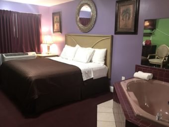 King bed, night stand with bedside lamp, wall mounted art and mirror, jacuzzi with towels and mirrored splash back, carpet flooring