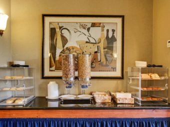 breakfast display with wall mounted art, with bagels, bread, breakfast pastries, cereal dispensers, utensils and plates
