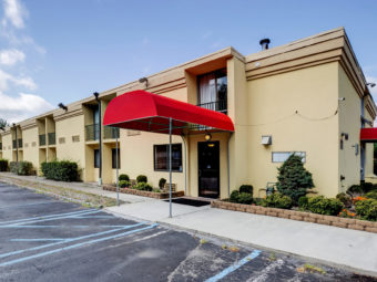 Hotel exterior with canopied entrance, landscaping and parking area