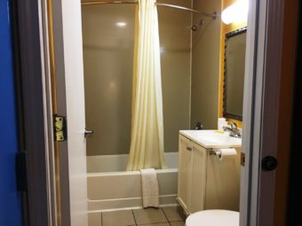 Shower tub with shower curtain, vanity unit, wall mounted mirror with overhead strip light, tiled flooring