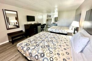 Two queen beds, night stand with bedside lamp, wooden bench, mirror, wooden unit with microwave, fridge, TV, desk with chair, hanging rail with hangers, portable folding luggage rack, laminate flooring