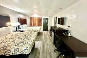 Two queen beds, night stand with bedside lamps and telephone, wooden bench, mirror, wooden unit with fridge and microwave, TV, desk with chair and coffeemaker, laminate flooring