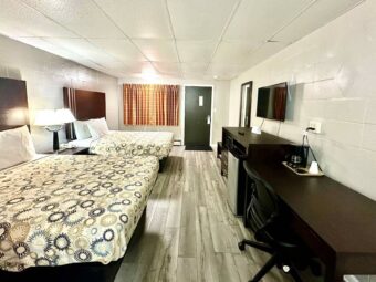 Two queen beds, night stand with bedside lamps and telephone, wooden bench, mirror, wooden unit with fridge and microwave, TV, desk with chair and coffeemaker, laminate flooring