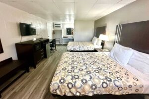 Two queen beds, night stand with bedside lamp, wooden bench, mirror, wooden unit with microwave, fridge, TV, desk with chair, hanging rail with hangers, portable folding luggage rack, laminate flooring