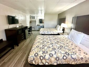 Two queen beds, night stand with bedside lamp, wooden bench, mirror, wooden unit with microwave, fridge, TV, desk with chair, hanging rail with hangers, portable folding luggage rack, laminate flooring