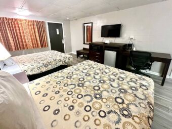 Two queen beds, night stand with bedside lamp, wooden bench, mirror, wooden unit with microwave, fridge, TV, desk with chair and coffee maker, laminate flooring