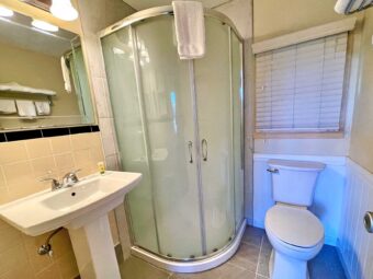 sink, mirror, toilet, corner shower with sliding doors, towels, tiled flooring