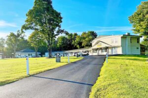 Hotel entrance drive, two story building, grassy areas, trees, parking spaces