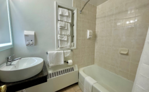 Vanity unit, illuminated mirror, towel rails with towels, shower tub with bath mat and shower curtain, tiled flooring