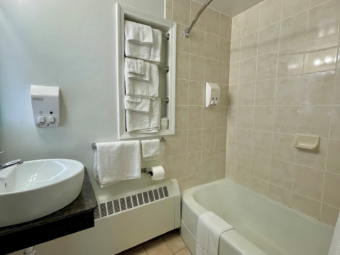 Vanity unit, illuminated mirror, towel rails with towels, shower tub with bath mat and shower curtain, tiled flooring