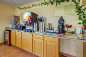 breakfast display counter with cereal dispensers, waffle iron, juice dispenser, coffee pot, fresh fruit, breakfast pastries, tiled flooring