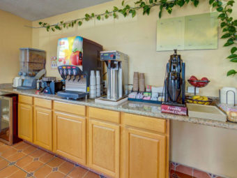 breakfast display counter with cereal dispensers, waffle iron, juice dispenser, coffee pot, fresh fruit, breakfast pastries, tiled flooring