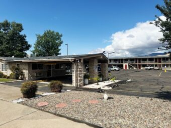 Hotel entrance with canopied entrance, two story building exterior guest room entrances, parking spaces, small bushes and graveled area