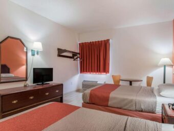 Wooden drawer unit with TV, mirror, wall light, hanging rail with hangers, table with chairs, floor lamp, two double beds, night stand with telephone, laminate flooring