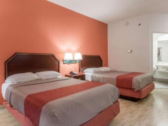 Two double beds, bedside wall lamps, night stand with telephone, doorway to bathroom with vanity unit and mirror, laminate flooring