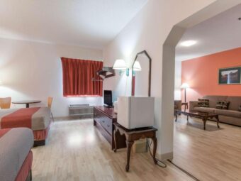Two double beds, night stand with telephone, bedside wall lights, floor lamp, table with chairs, wooden drawer unit, hanging rail with hangers, wall light, table with fridge, archway to sitting area, sofa, occasional table, floor lamp, art image, laminate flooring