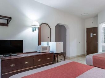 Hanging rail, wooden drawer unit with TV and microwave, wall lamp, mirror, table with fridge, archway to sitting room, doorway to bathroom