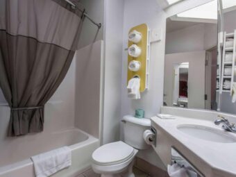 Vanity unit, mirror, stand with towels, shower tub with shower curtain and bath mat, toilet