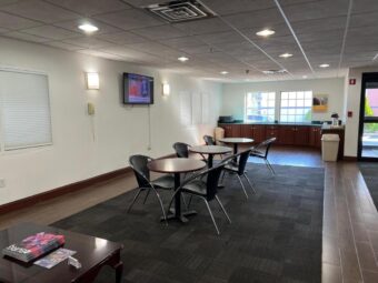 Tables and chairs, wall mounted TV, breakfast preparation area, waste bin, tiled and carpet flooring
