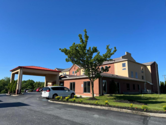 Hotel entrance with canopied drive through entrance, two story building. landscaping with grassy areas, flowers and small trees.