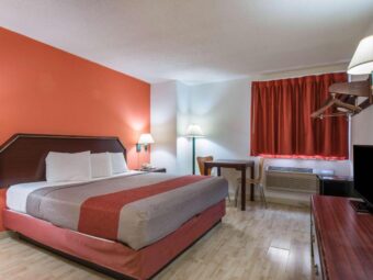 King bed. night stand with telephone, bedside wall light, floor lamp, table and chairs, fridge, hanging rail with hangers, wooden drawer unit with TV, aminate flooring