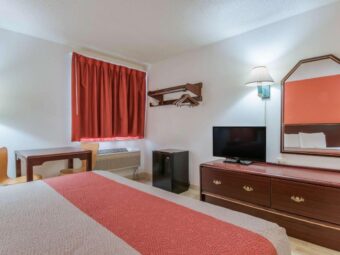 table and chairs, hanging rail with hangers and iron holder, fridge, wooden drawer unit with TV, wall lamp, mirror, folding portable luggage rack, king bed, laminate flooring,