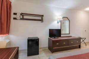 Hanging rail with hangers and iron holder, fridge, wooden drawer unit with TV, wall lamp, mirror, folding portable luggage rack, king bed, laminate flooring