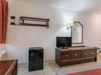 Hanging rail with hangers and iron holder, fridge, wooden drawer unit with TV, wall lamp, mirror, folding portable luggage rack, king bed, laminate flooring