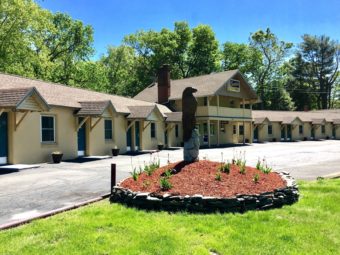 One story building, exterior room entrances, parking spaces, grassy area, flower bed with statue